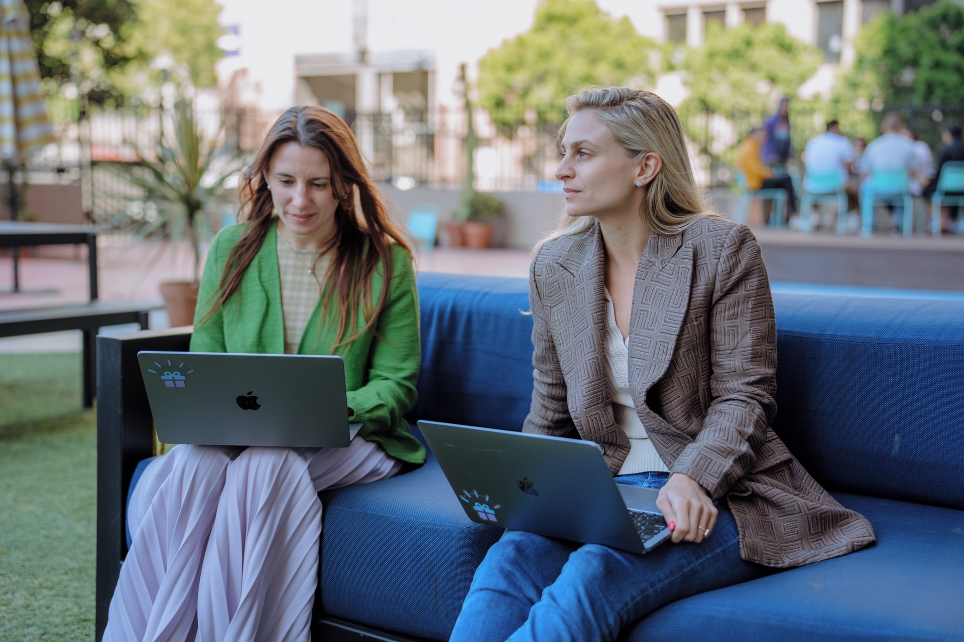 Two women sitting on a couch with laptops